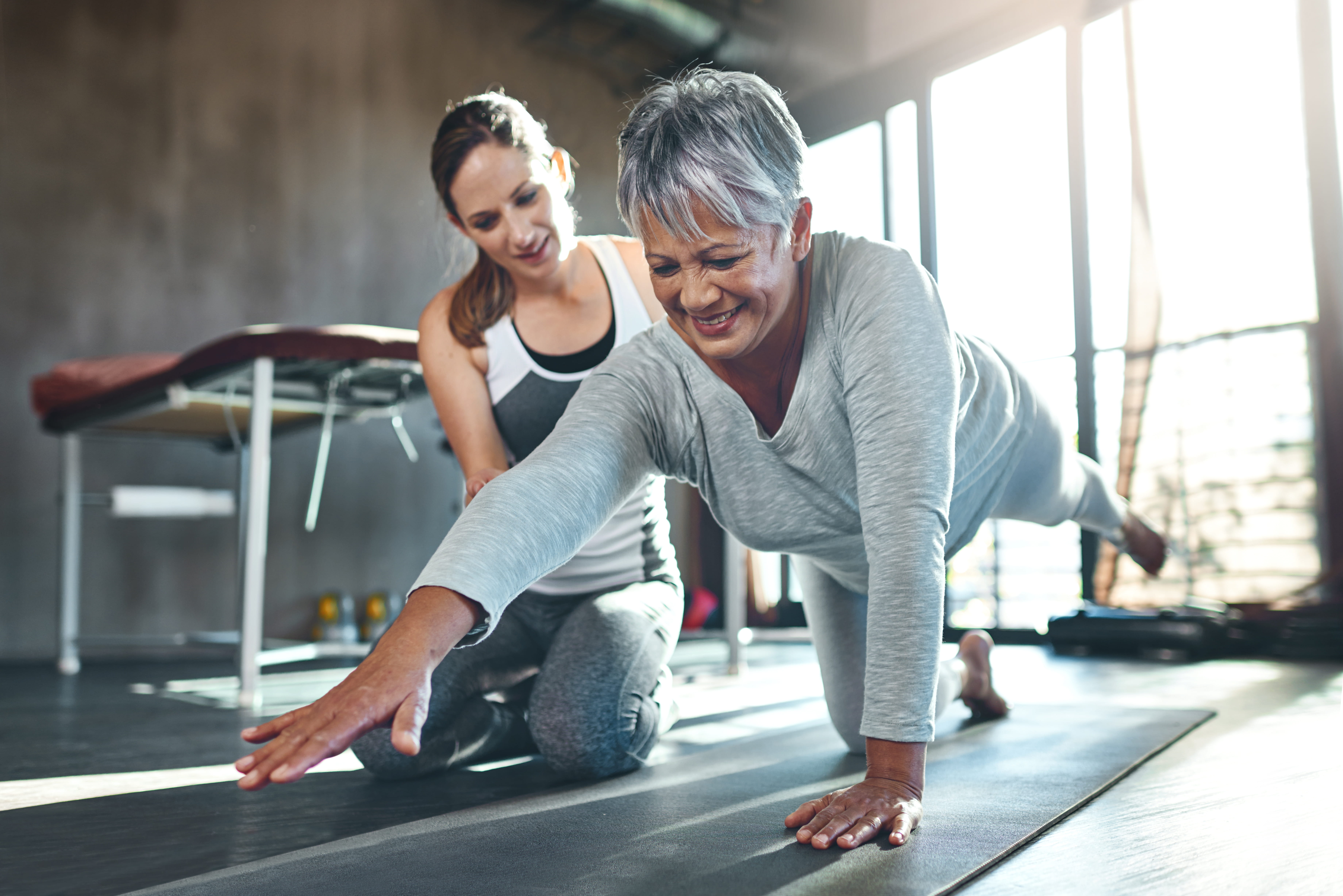 Senior woman practices yoga with a personal trainer in a gym.