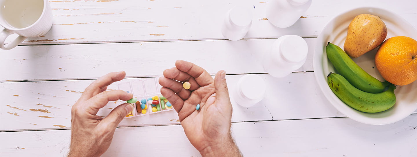 Hands holding pills next to a bowl of fruit