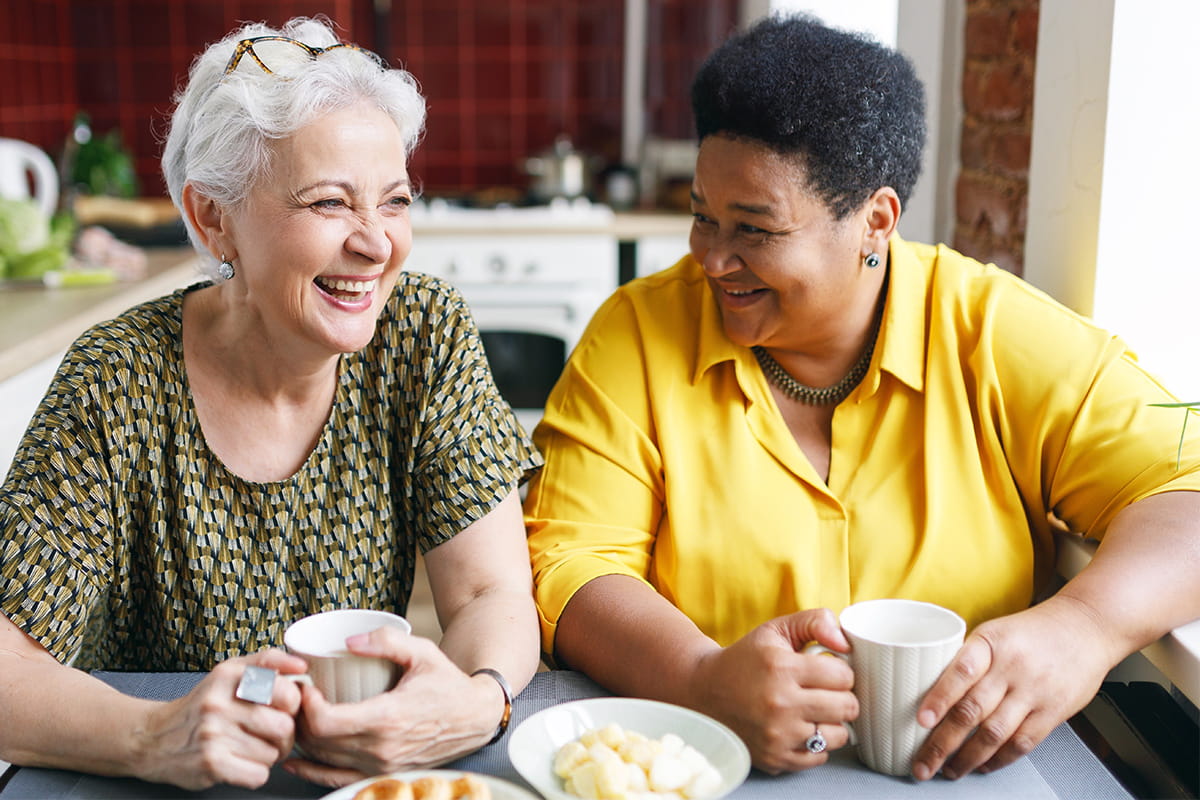 Two senior women smile and chat over coffee.