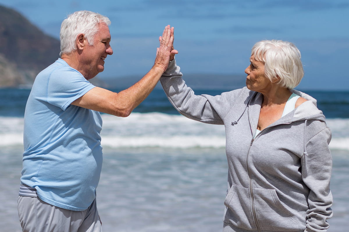 Senior man and woman high-five at the beach.