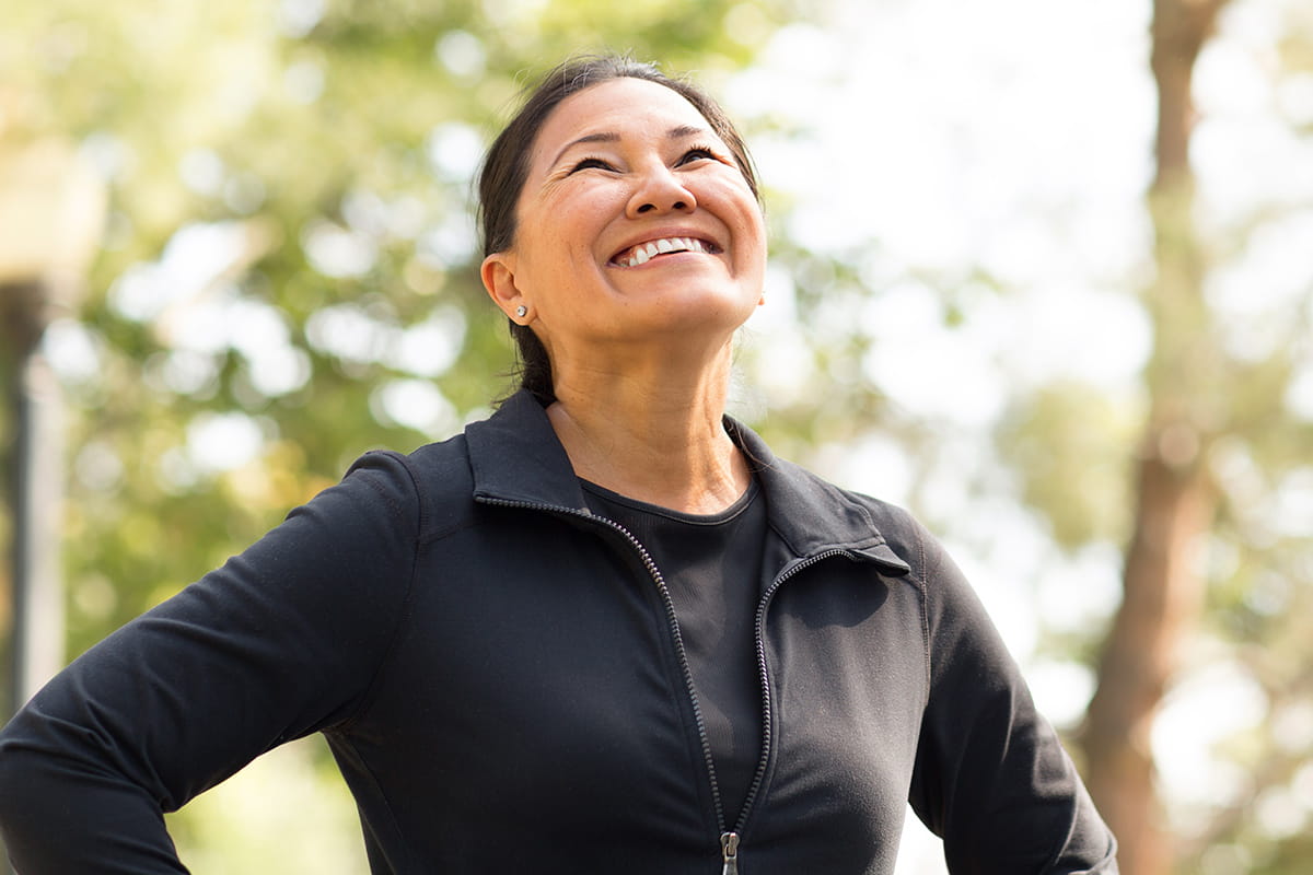 Person in dark jogging attire smiles toward the sky while exercising outside.
